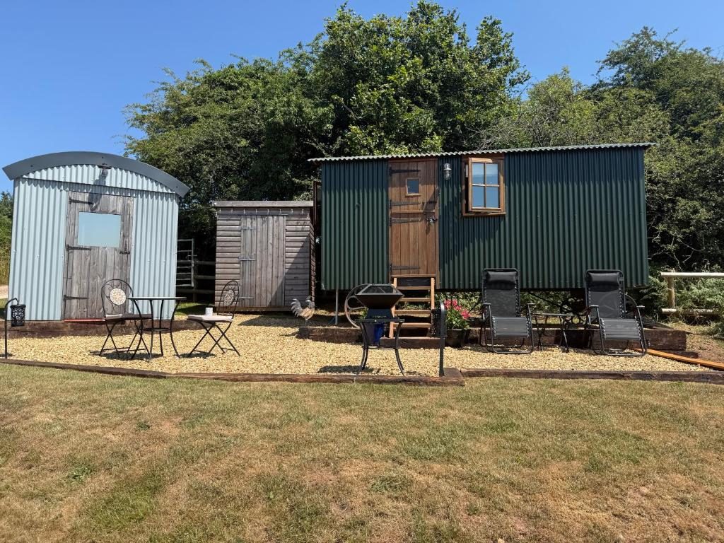 The green shepherd hut and its shower-room hut on a sunny day, with a cockerel on the gravel